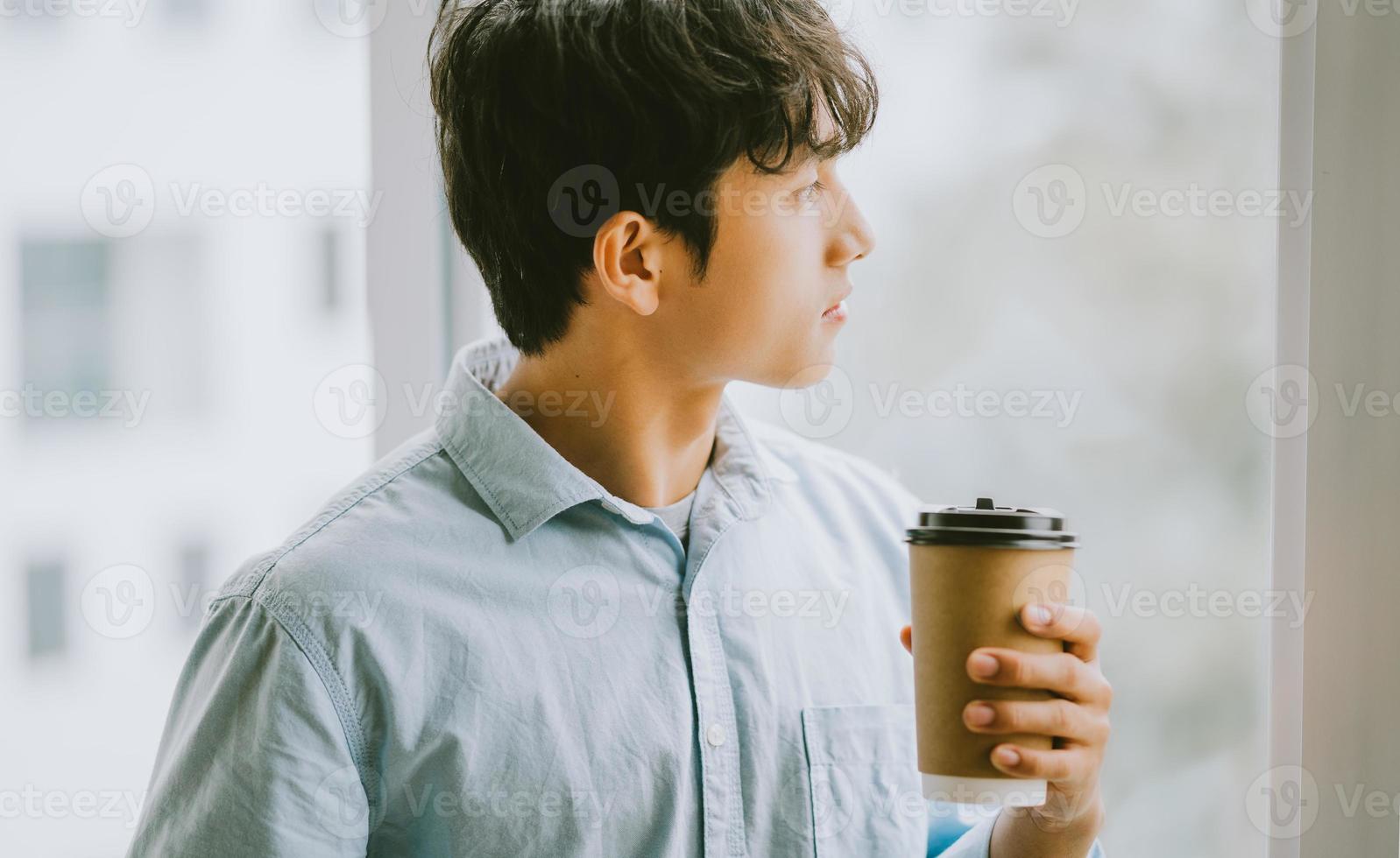 uomo d'affari asiatico sta bevendo caffè vicino alla finestra foto