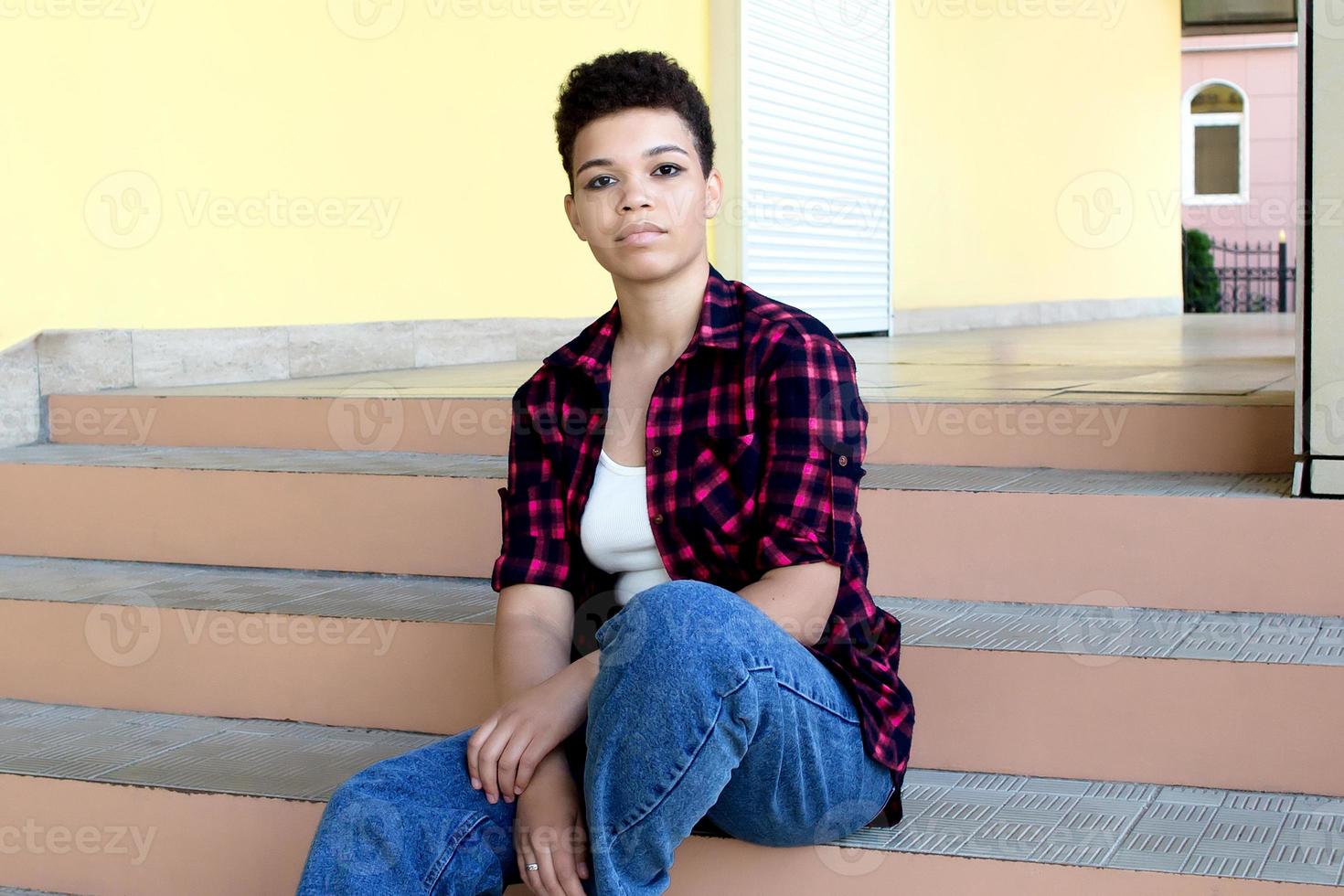 bella donna afroamericana con i capelli corti, seduta fuori sulle scale, stile di vita foto