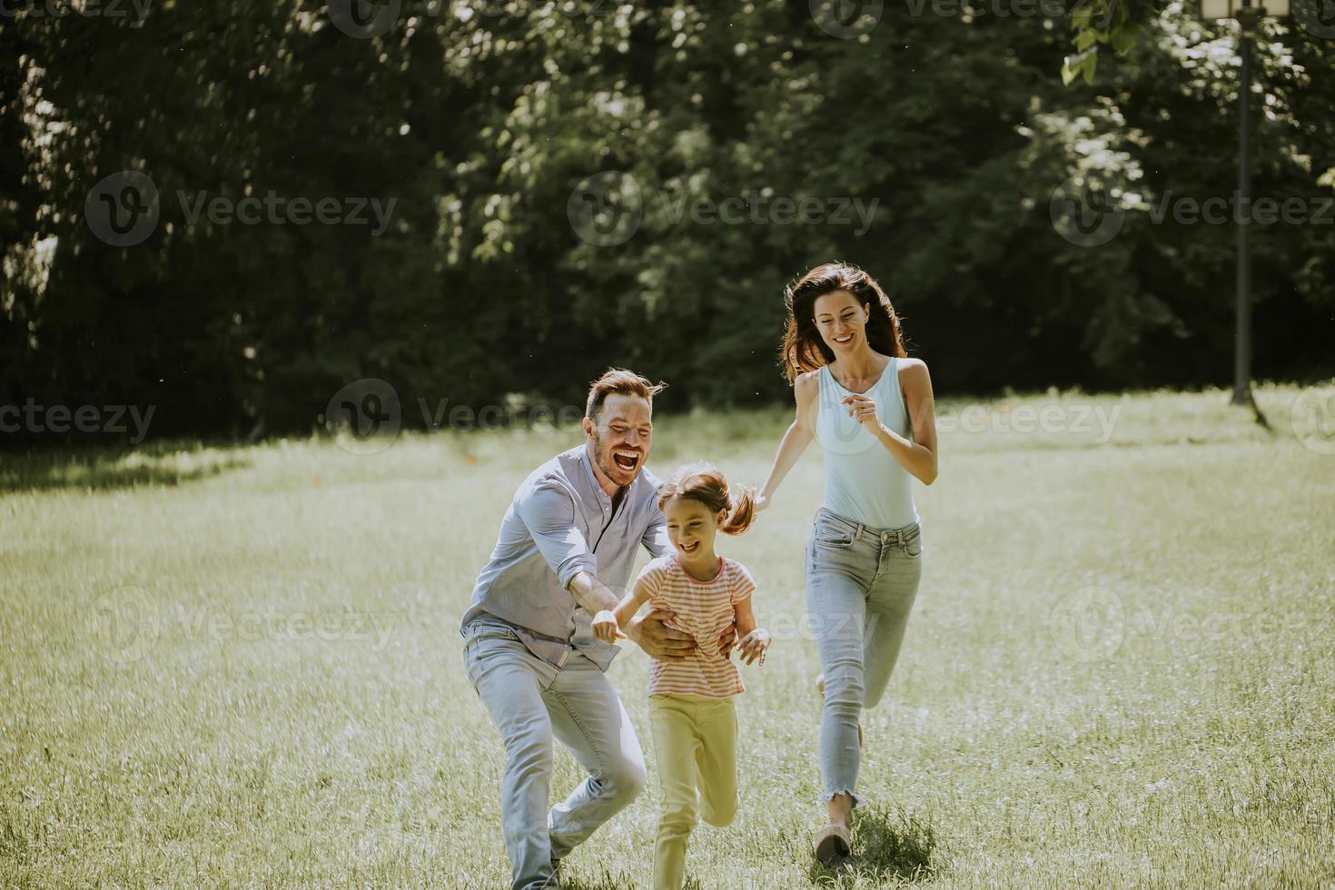 giovane famiglia felice con la piccola figlia carina che corre nel parco in una giornata di sole foto