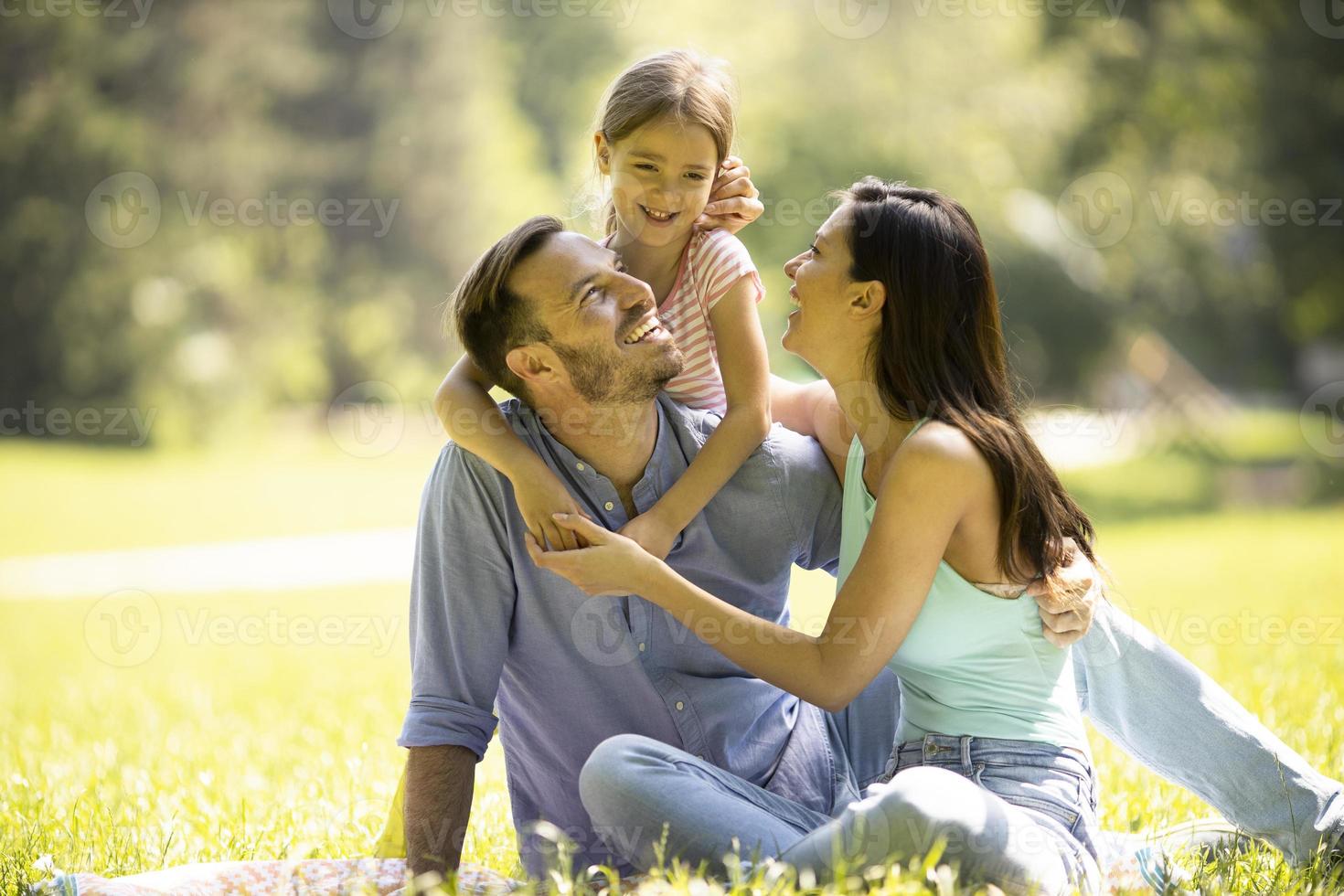 giovane famiglia felice con la piccola figlia carina che si diverte nel parco in una giornata di sole foto