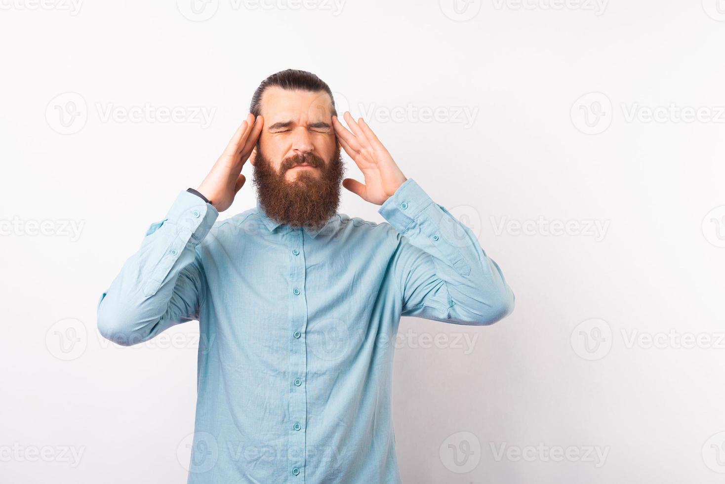 foto di un uomo barbuto in camicia blu con emicrania, duro lavoro d'ufficio