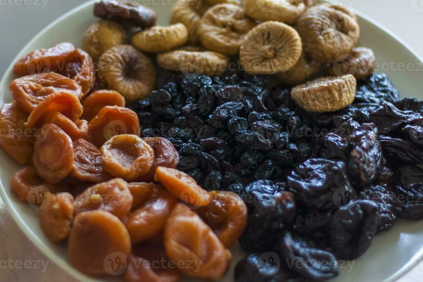 Uomini mani hold un' piatto di secco frutta al di sopra di il tavolo. prugne, secco albicocche, fichi, uva passa su un' grande piatto. foto