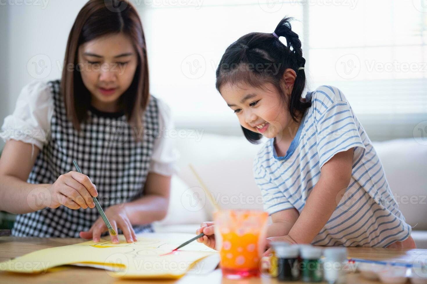 carino poco bambino pittura con colorato vernici. asiatico ragazza e madre utilizzando pastello disegno colore. figlia e mamma fare compiti a casa colorazione cartone animato personaggi. bambino artista attività stile di vita concetto. foto