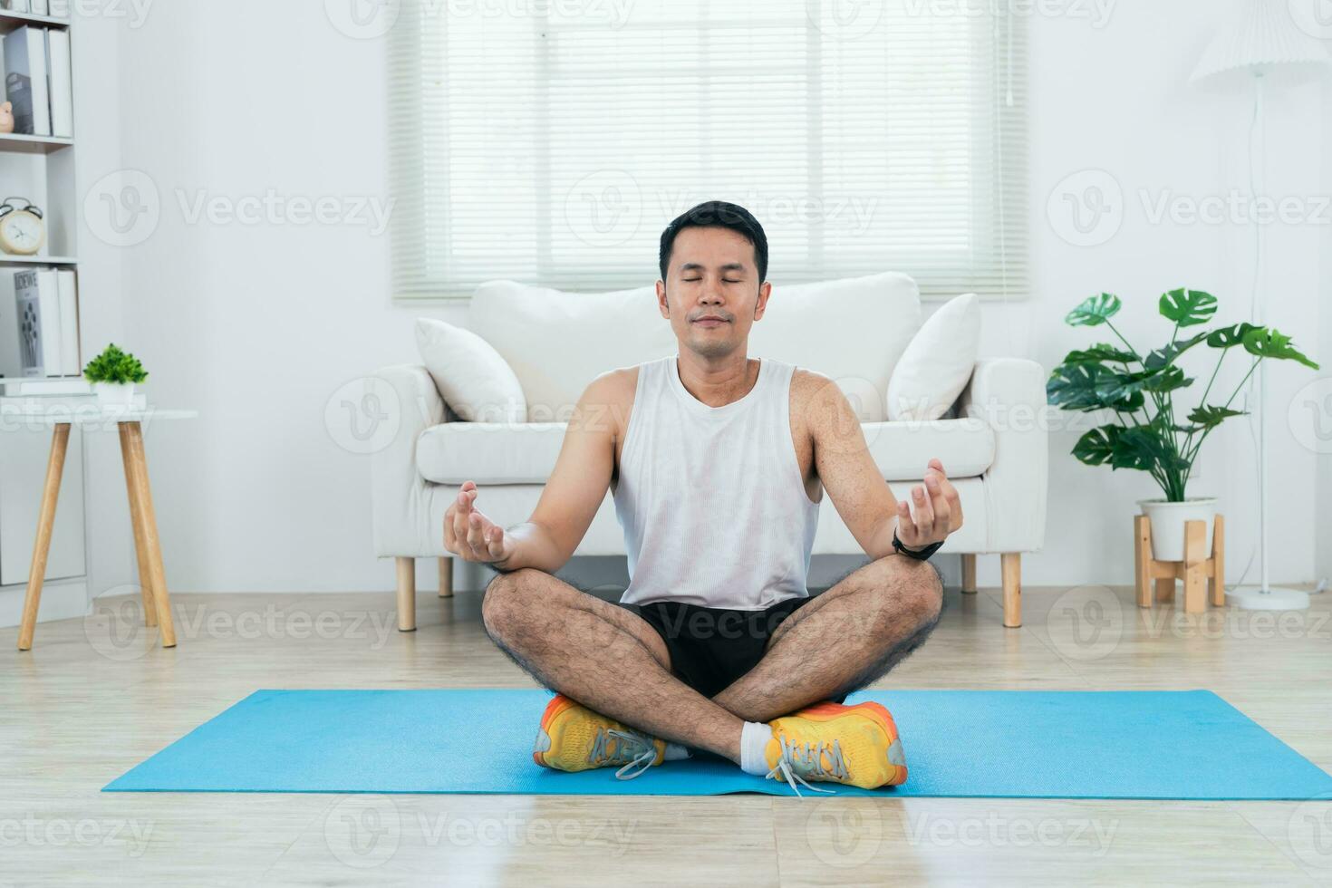 in linea classe addestramento. contento asiatico maturo uomo nel abbigliamento sportivo fabbricazione allungamento per gambe su stuoia yoga e meditare nel vivente camera interno e sorridente. contento sportivo allenarsi di lui slef. sport a casa. foto