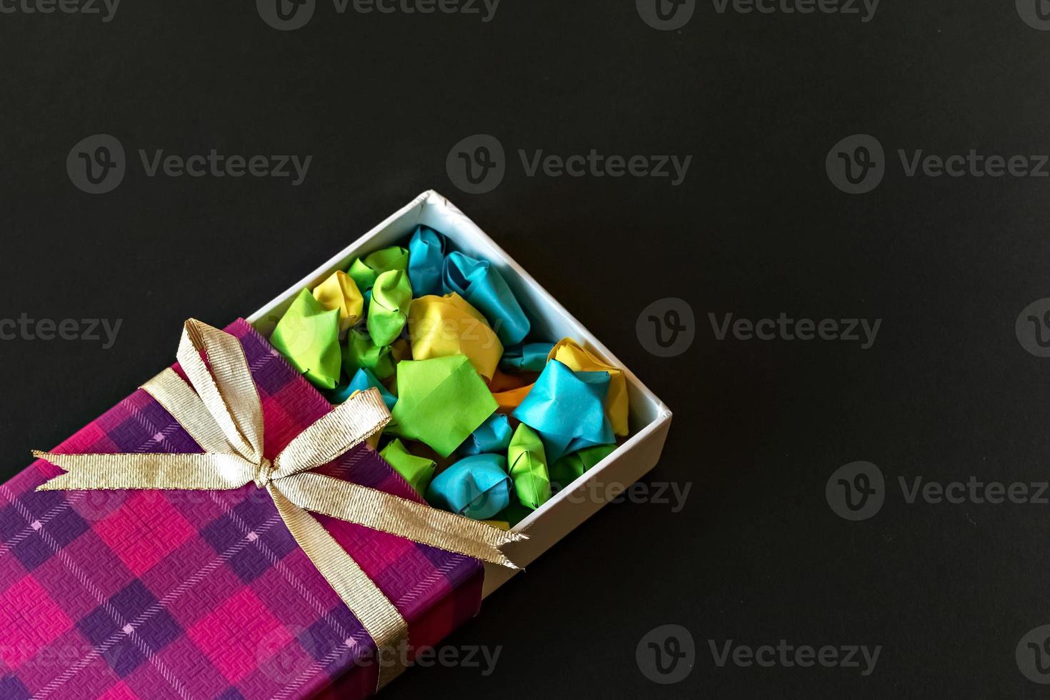 confezione regalo colorata con fiocco in raso con stelle di carta origami su sfondo nero. regali per le feste. foto
