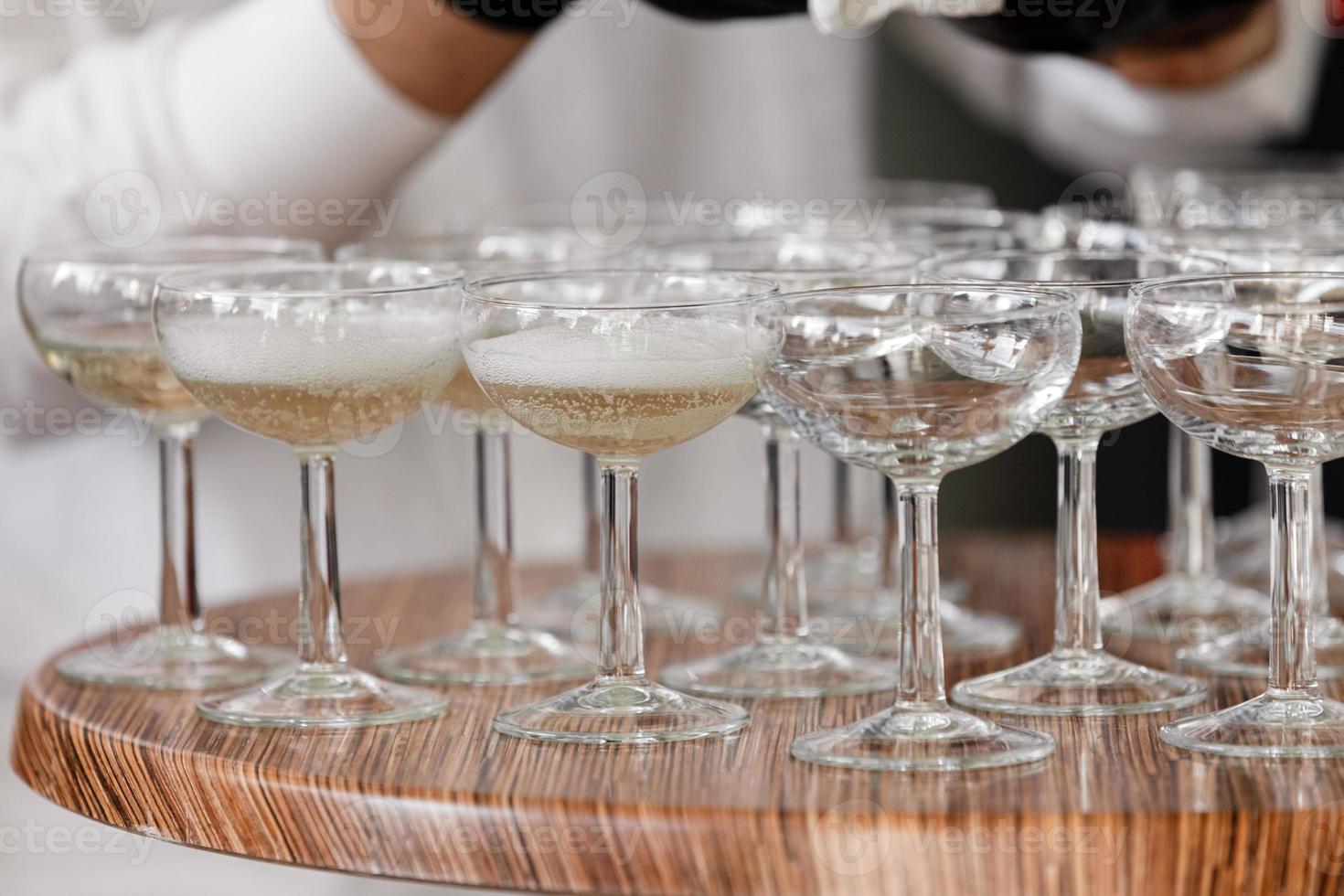 spumante, champagne in bicchieri sul tavolo di legno. cameriere in guanti neri versa l'alcol nei bicchieri nel ristorante. messa a fuoco selettiva foto