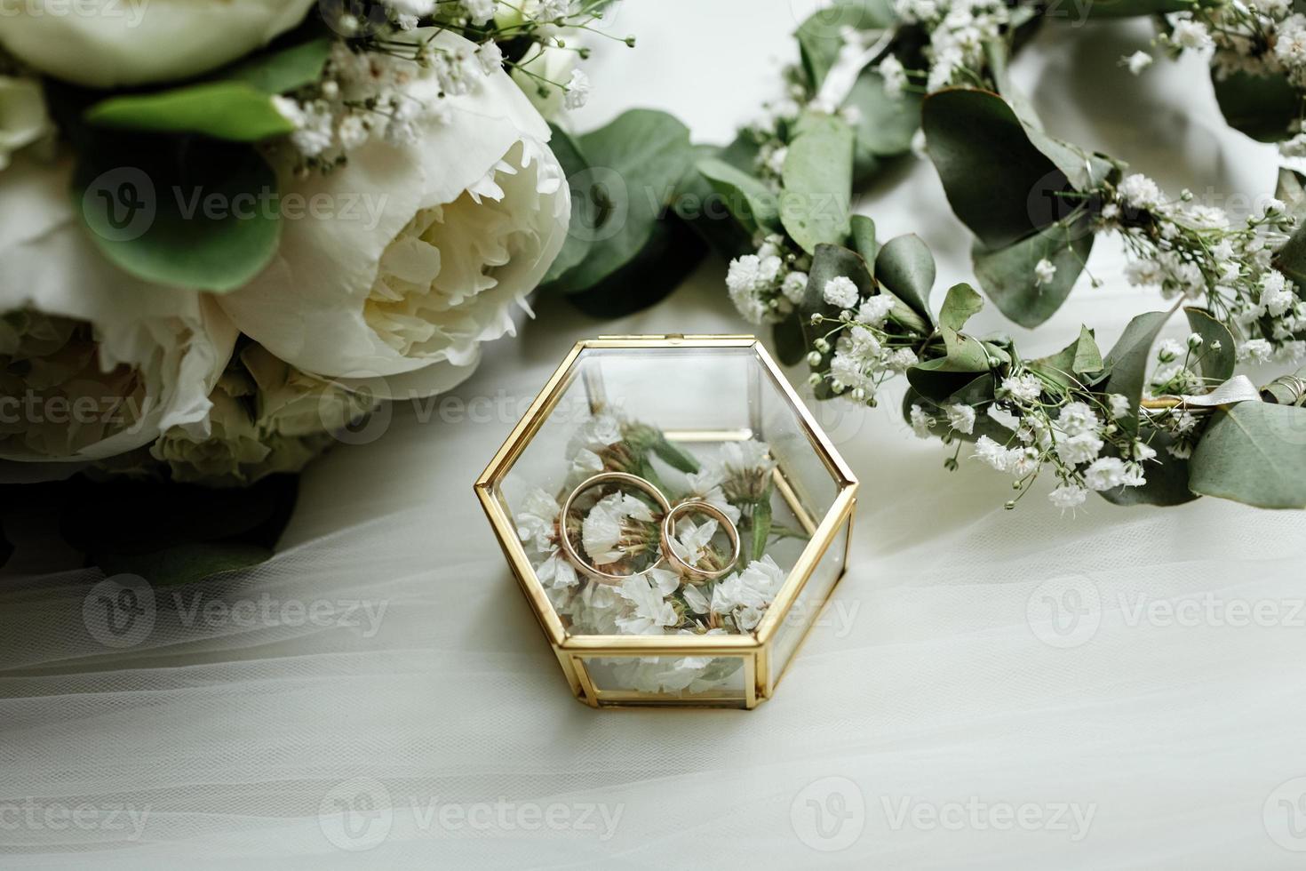 dettagli del matrimonio. due classiche fedi nuziali in oro in una scatola di vetro e un bouquet di fiori bianchi e verde foto