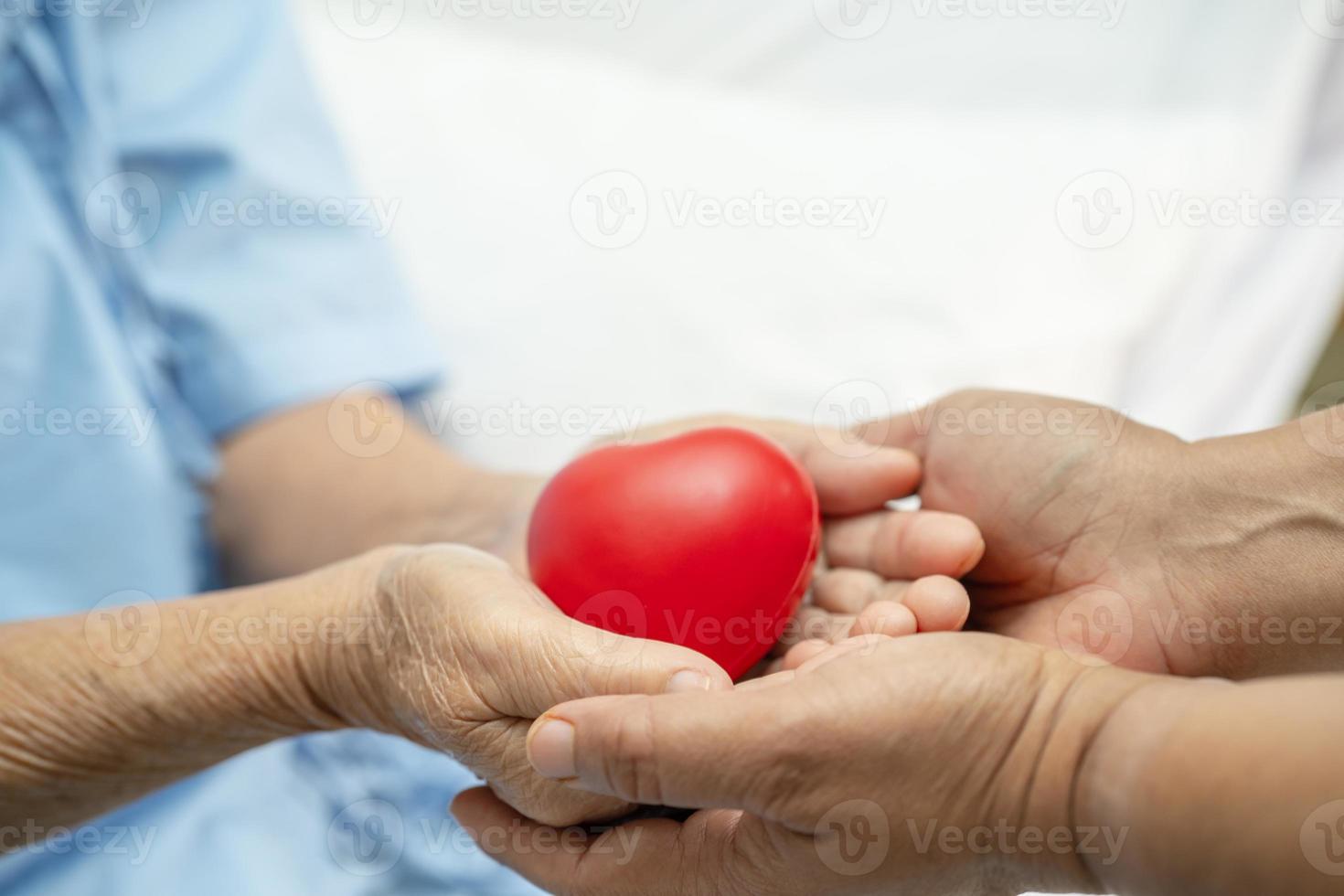 paziente asiatico anziana o anziana donna anziana che tiene il cuore rosso in mano sul letto nel reparto ospedaliero di cura, concetto medico sano e forte foto