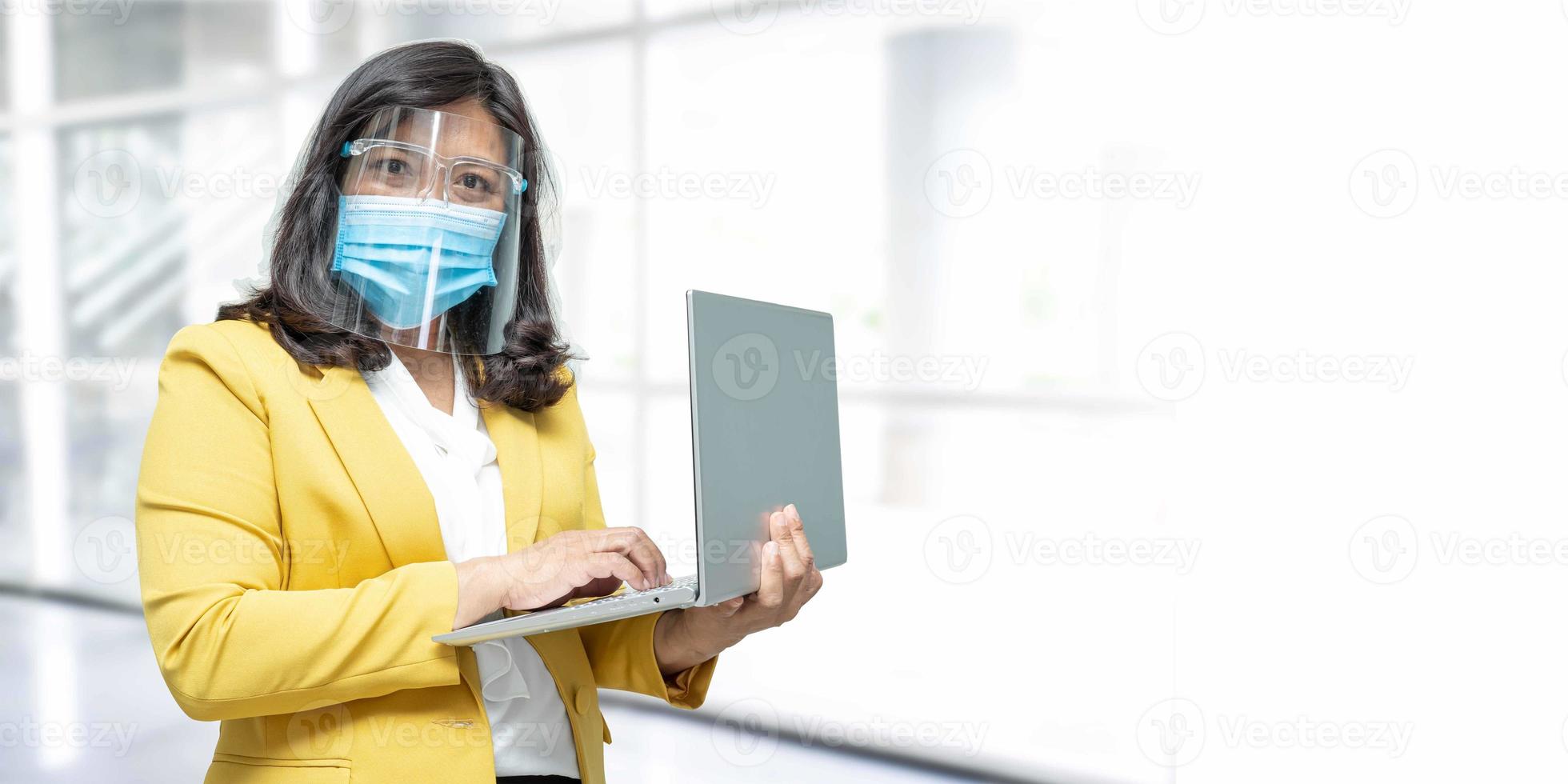 signora asiatica di affari che indossa la maschera per il viso che tiene il computer portatile in ufficio con lo spazio della copia. foto