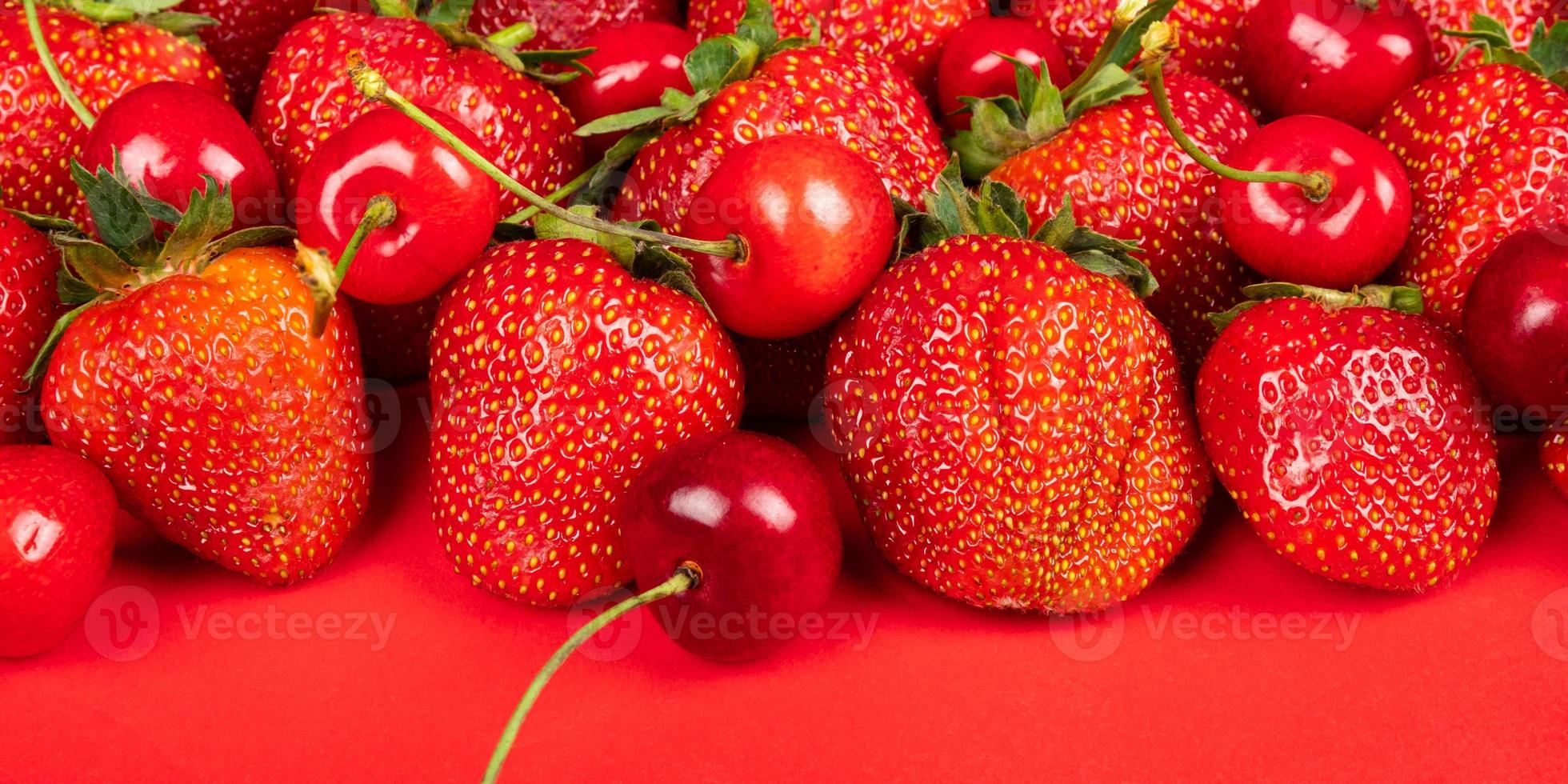primo piano di ciliegie e fragole su uno sfondo rosso foto