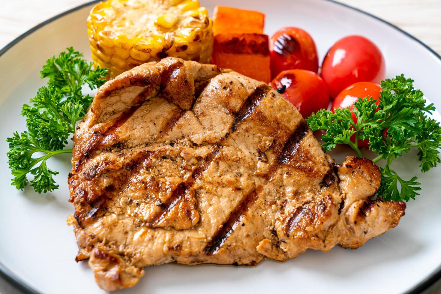 Filetto di maiale alla griglia e alla brace con mais, carota e pomodori foto