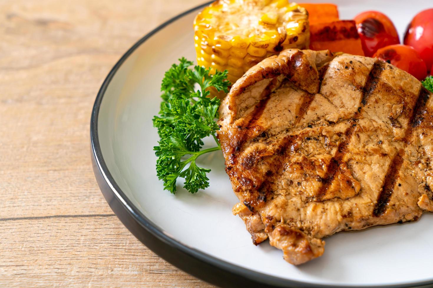 Filetto di maiale alla griglia e alla brace con mais, carota e pomodori foto