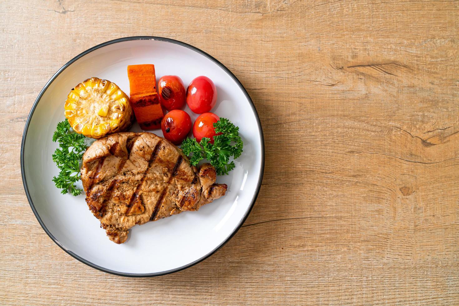 Filetto di maiale alla griglia e alla brace con mais, carota e pomodori foto