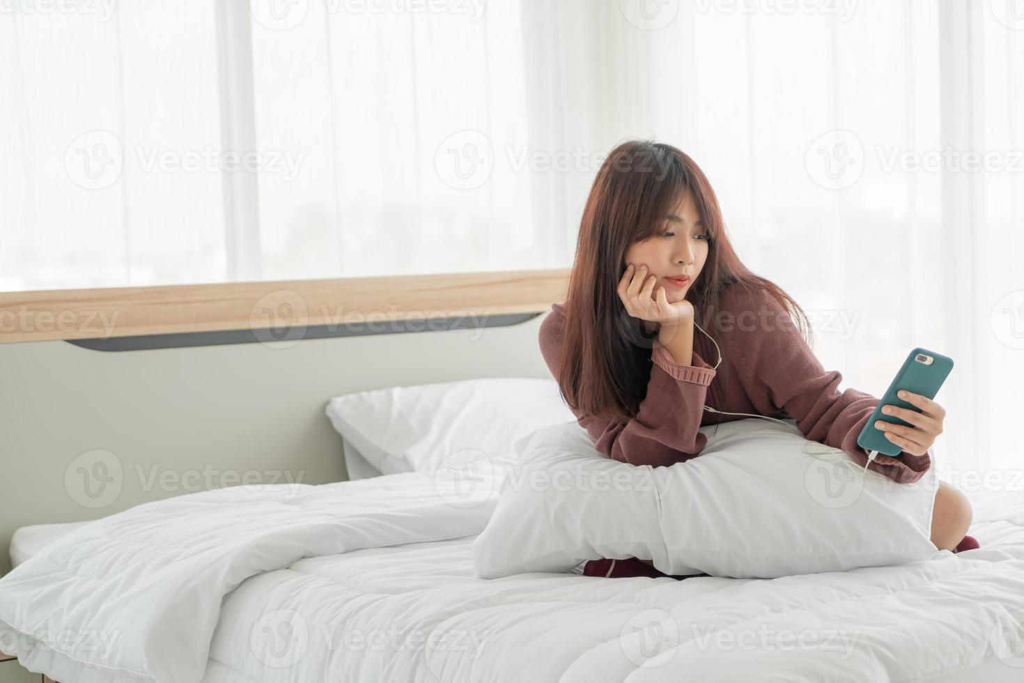 donna asiatica che gioca a smartphone sul letto foto