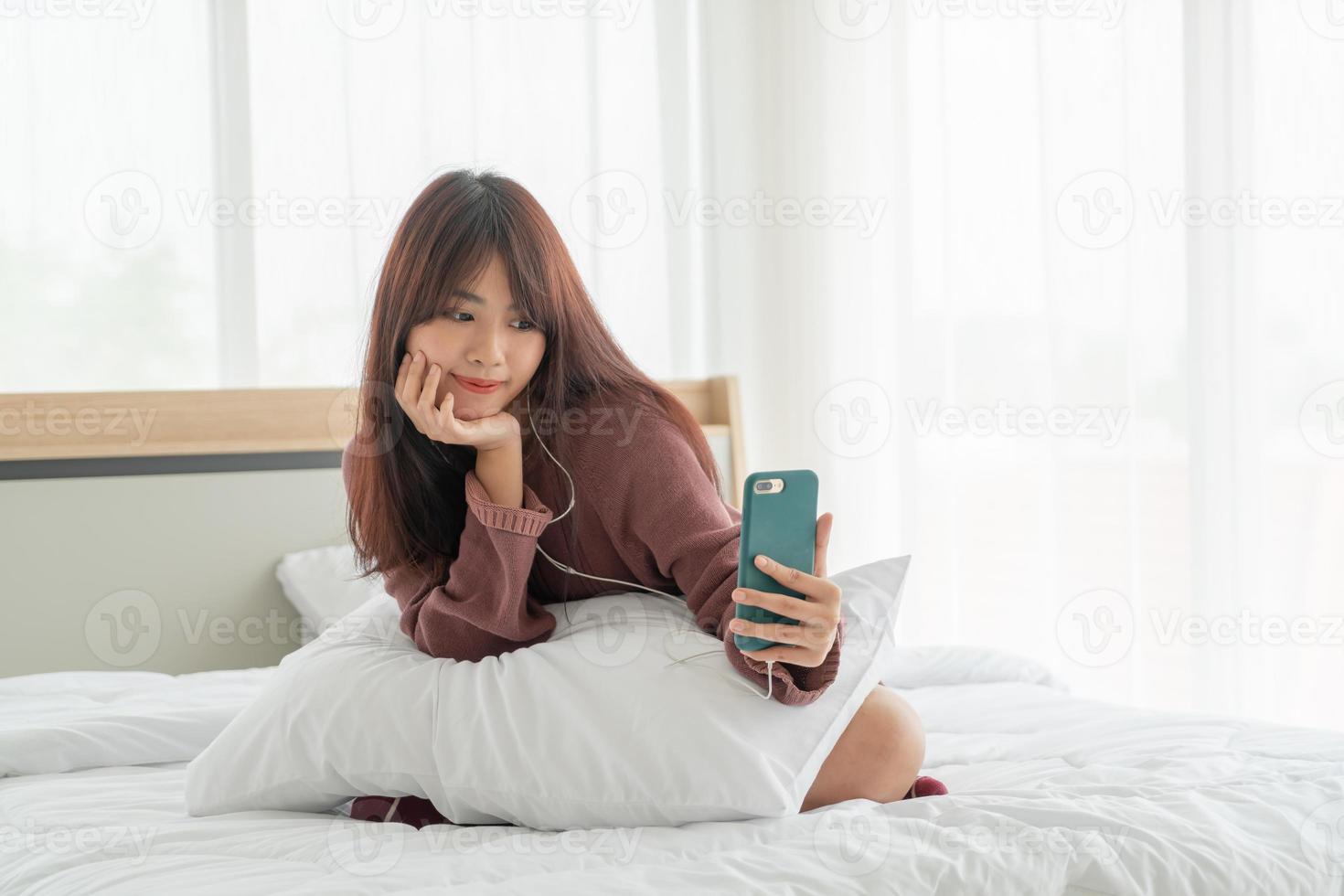 donna asiatica che gioca a smartphone sul letto foto