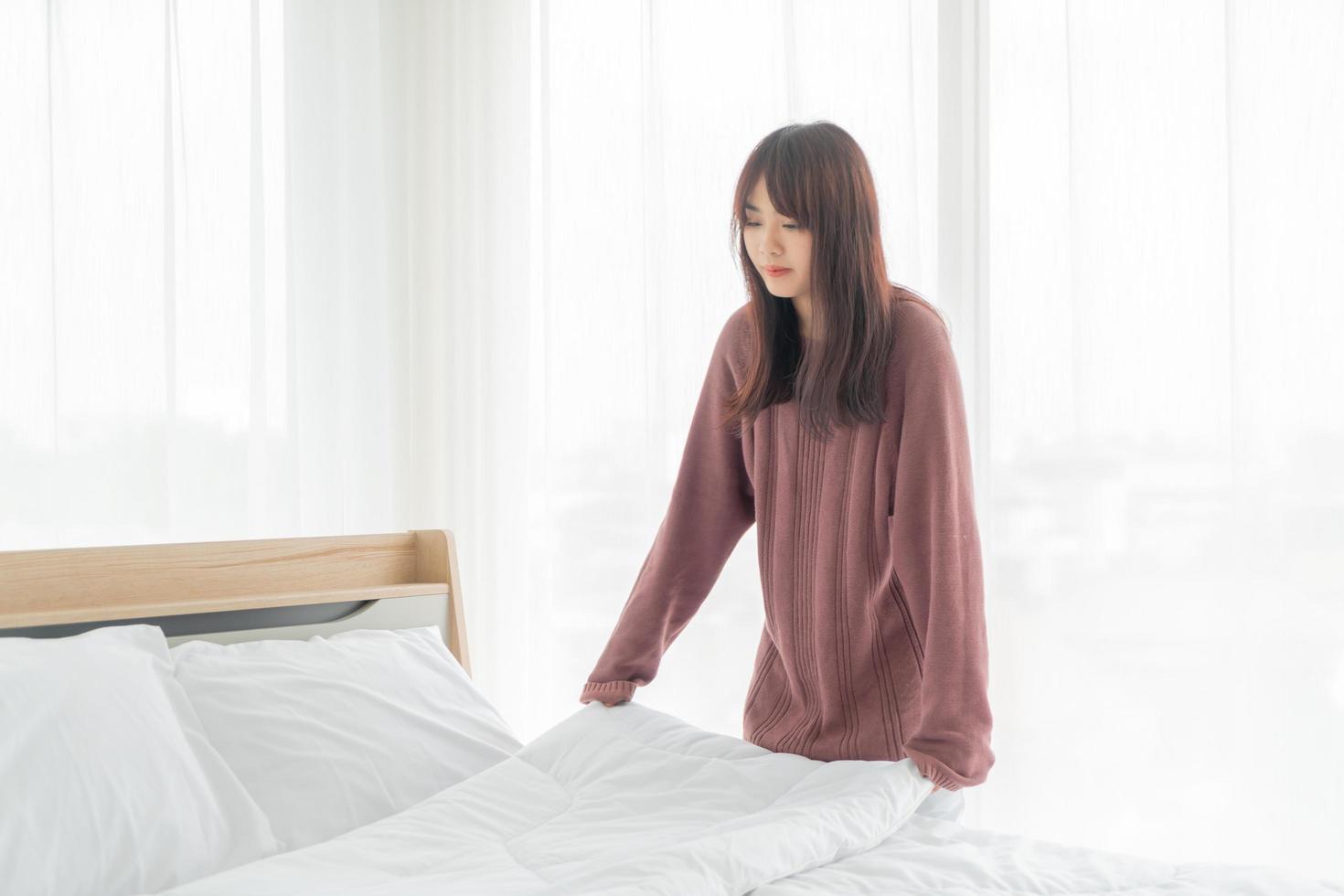 donna asiatica che fa il letto in camera con lenzuolo bianco pulito foto