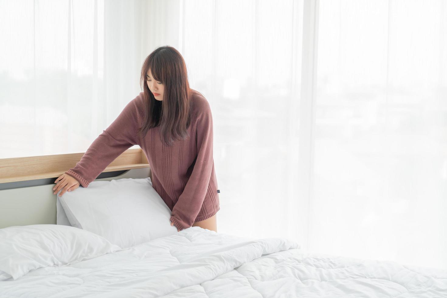 donna asiatica che fa il letto in camera con lenzuolo bianco pulito foto