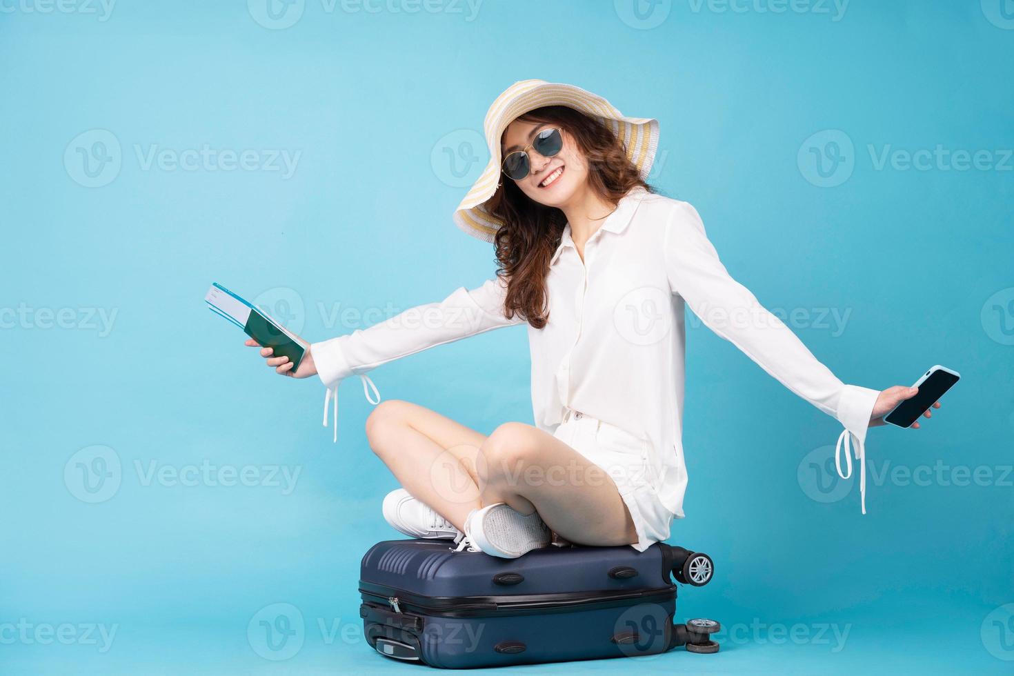 giovane donna asiatica che tiene biglietto aereo e telefono seduto sulla valigia? foto