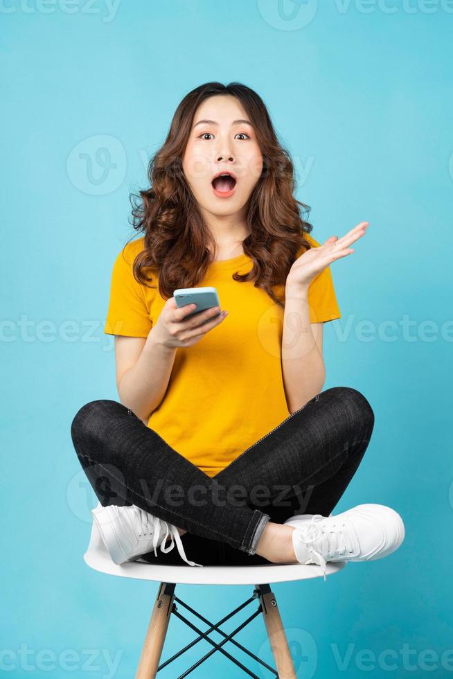 giovane donna asiatica seduta in poltrona usando il telefono con espressione sorpresa surprised foto