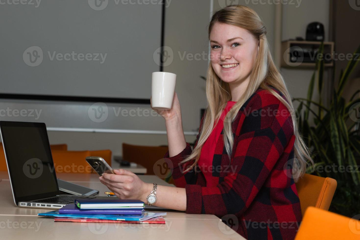 donna bionda sorridente che si siede a un computer portatile che beve tè e lavora. foto