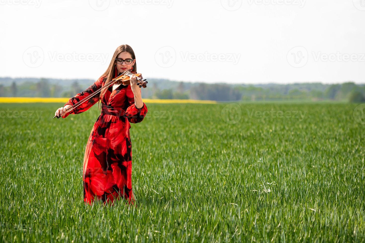 giovane donna in abito rosso suona il violino in un prato verde - immagine foto