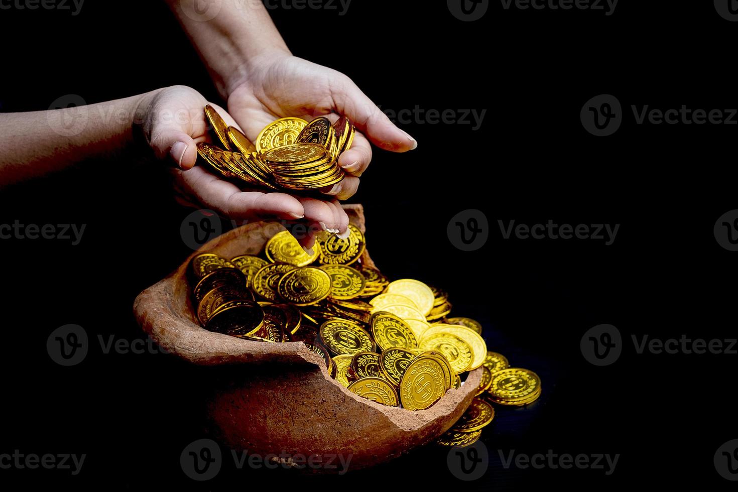 moneta d'oro in mano su lotti impilando monete d'oro in un vaso del tesoro rotto sfondo bianco foto