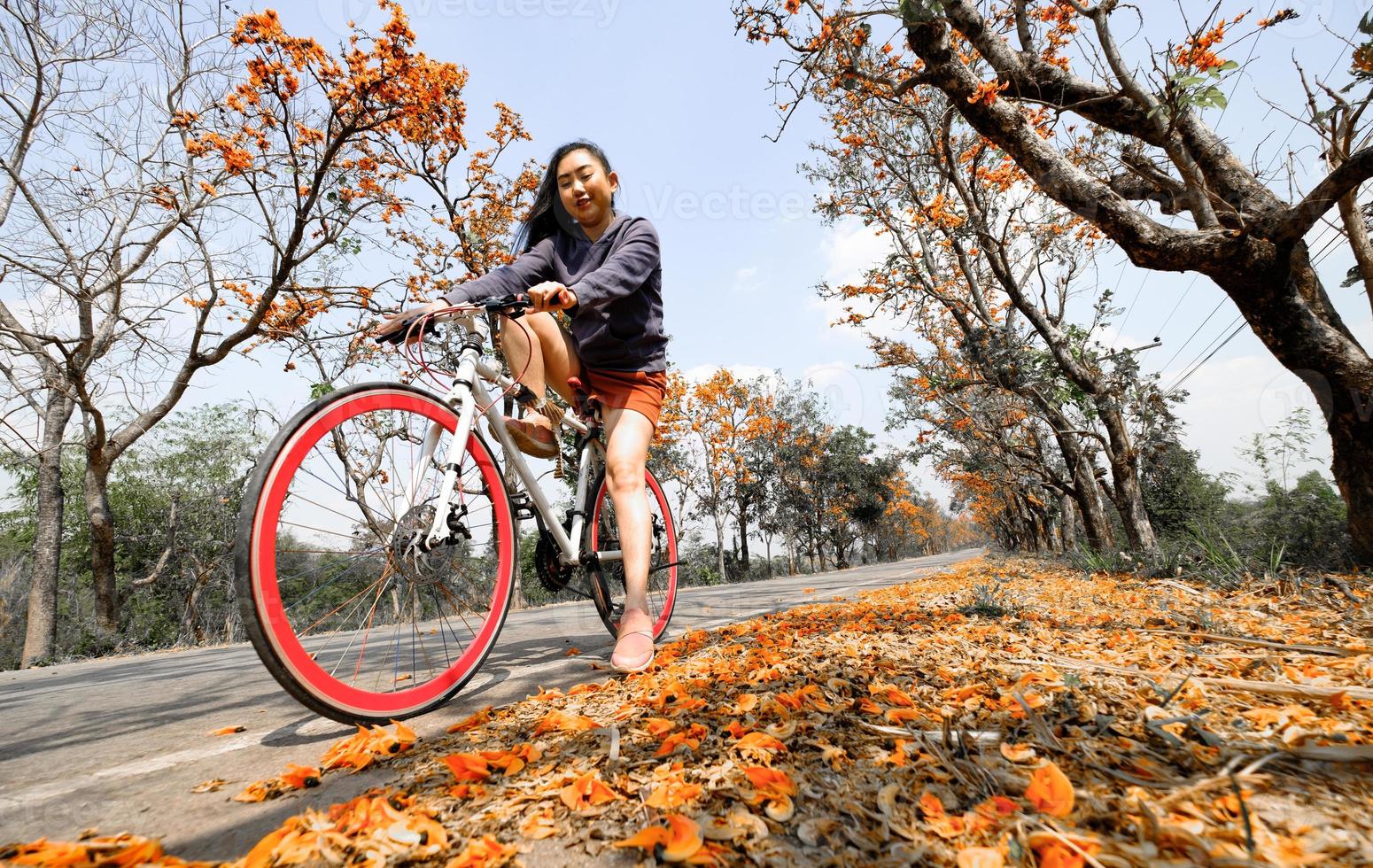 giovane donna felice di godersi l'attività di svago all'aperto in sella a una bicicletta e sorridendo per la felicità gli stili di vita sani pieni di bellissimi fiori d'arancio sullo sfondo foto
