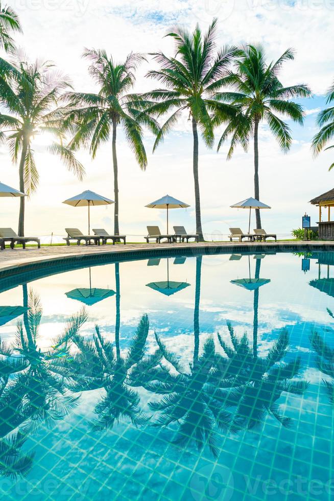 bellissimi ombrelloni e sedie di lusso intorno a una piscina all'aperto in hotel e resort con palme da cocco sul cielo al tramonto o all'alba - concetto di vacanza e vacanza foto