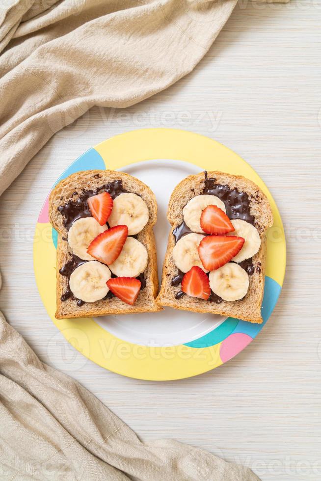 pane integrale tostato con banana fresca, fragola e cioccolato per colazione foto