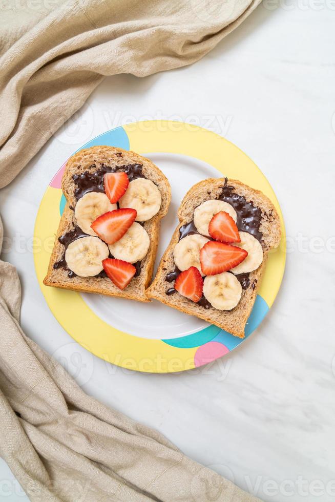 pane integrale tostato con banana fresca, fragola e cioccolato per colazione foto