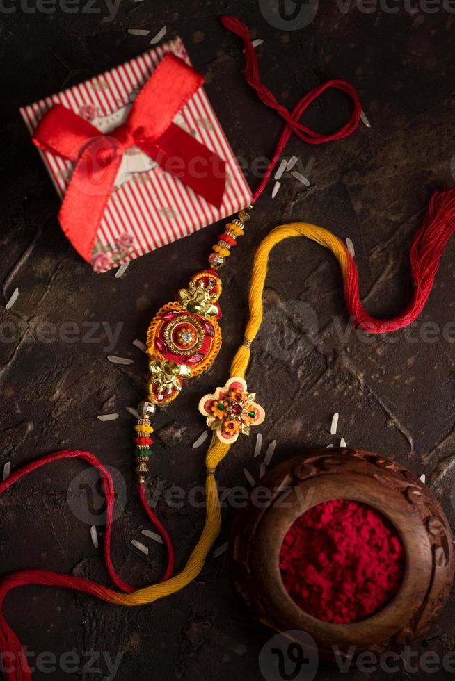 sfondo raksha bandhan con un elegante rakhi, chicchi di riso, kumkum e confezione regalo. un tradizionale cinturino da polso indiano che è un simbolo di amore tra fratelli e sorelle. foto