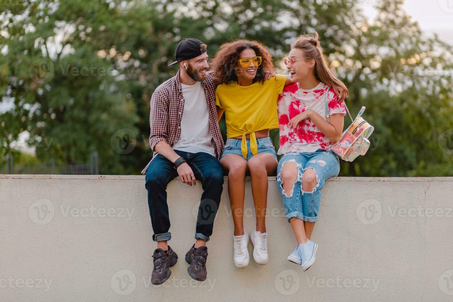 contento giovane azienda di sorridente amici seduta nel parco foto