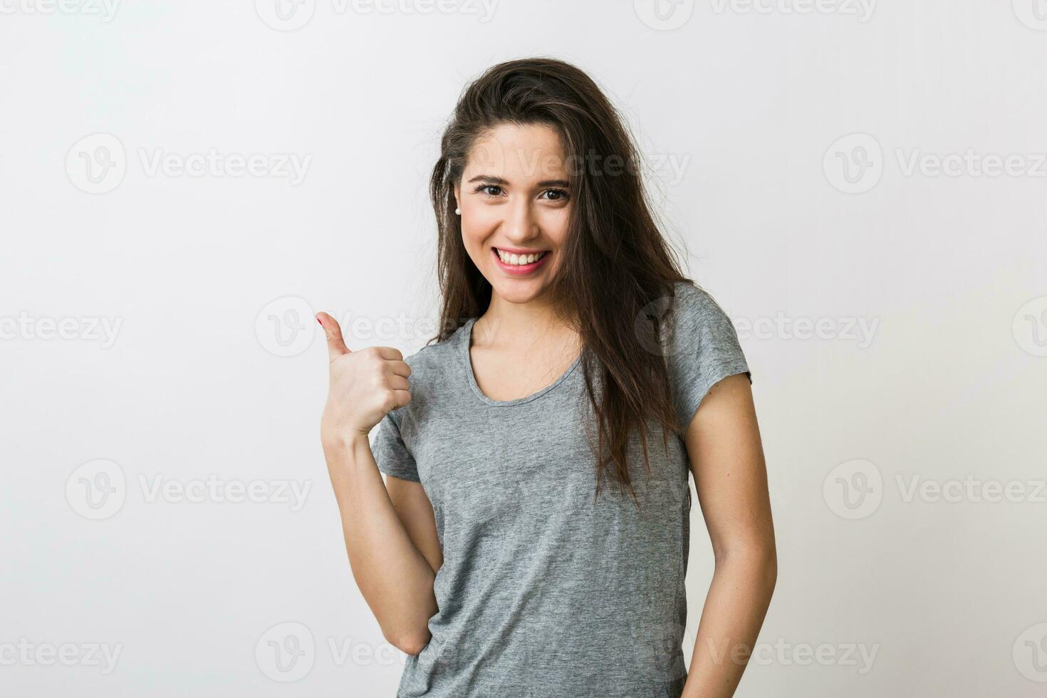 ritratto di elegante giovane bella donna sorridente nel grigio maglietta su bianca studio sfondo, isolato, mostrando pollice su, felice, positivo gesto foto