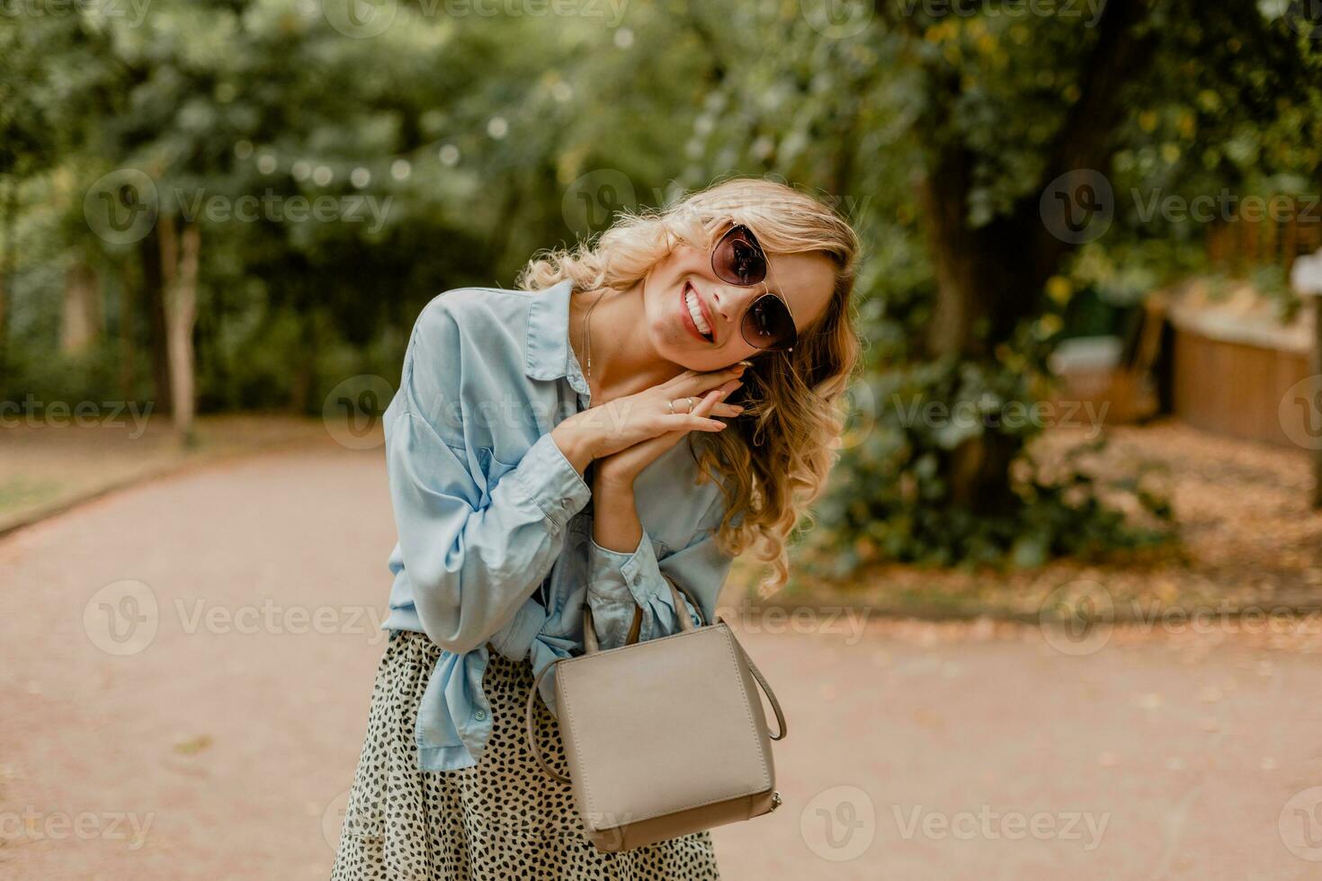 attraente biondo sorridente donna a piedi nel parco nel elegante attrezzatura foto
