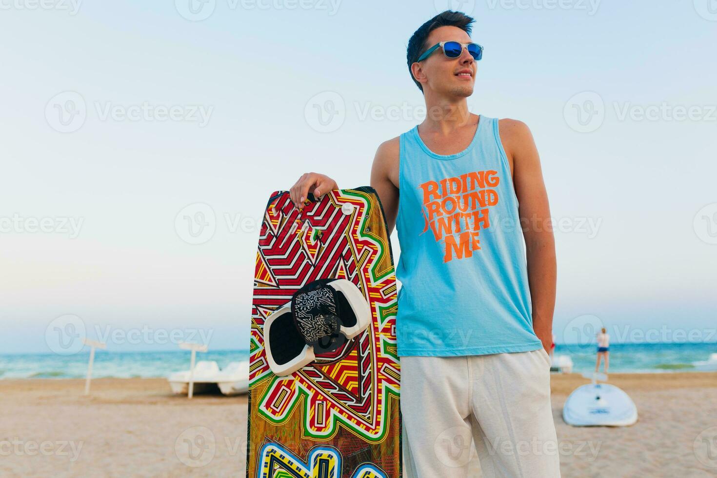 giovane atletico uomo con aquilone fare surf tavola in posa su spiaggia indossare occhiali da sole su estate vacanza, attivo gli sport passatempo foto
