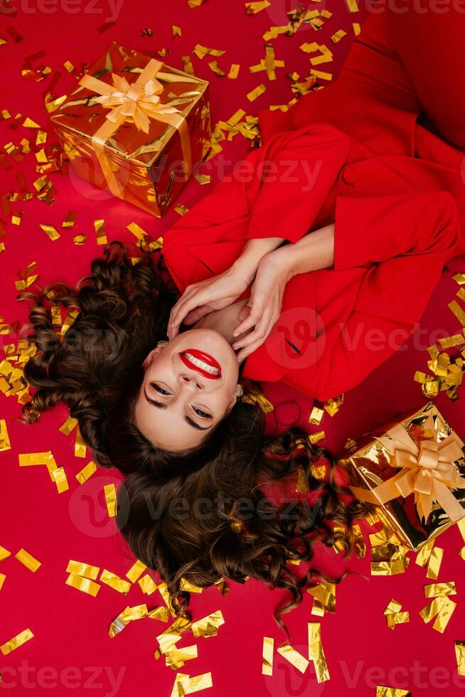 attraente donna festeggiare Natale su rosso sfondo nel coriandoli foto