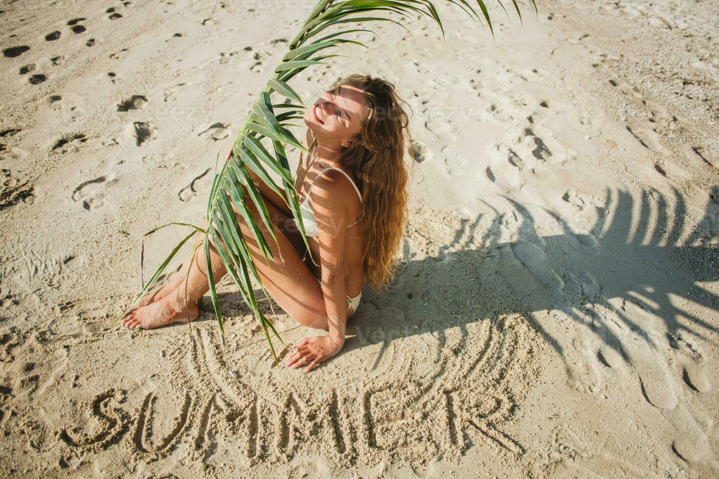 giovane magro donna nel bianca bikini costumi da bagno Tenere foglia di palma albero foto