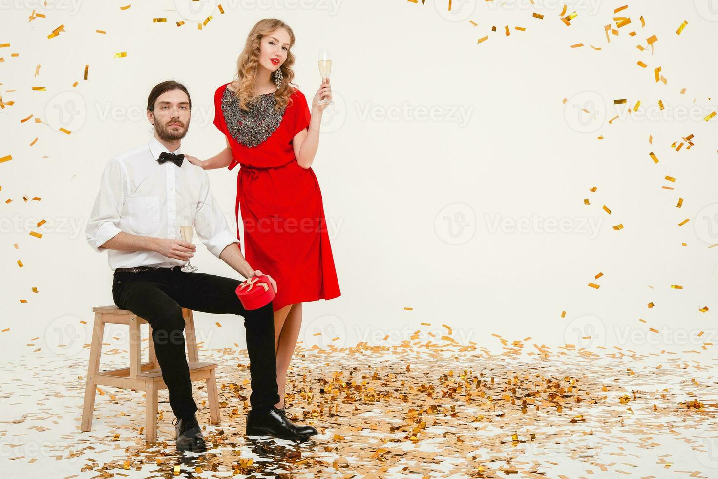 giovane elegante coppia nel amore su bianca sfondo Tenere bicchieri e potabile Champagne, festeggiare nuovo anno, indossare rosso vestire, moda gioielleria, arco legare, contento discoteca festa, avendo divertimento foto