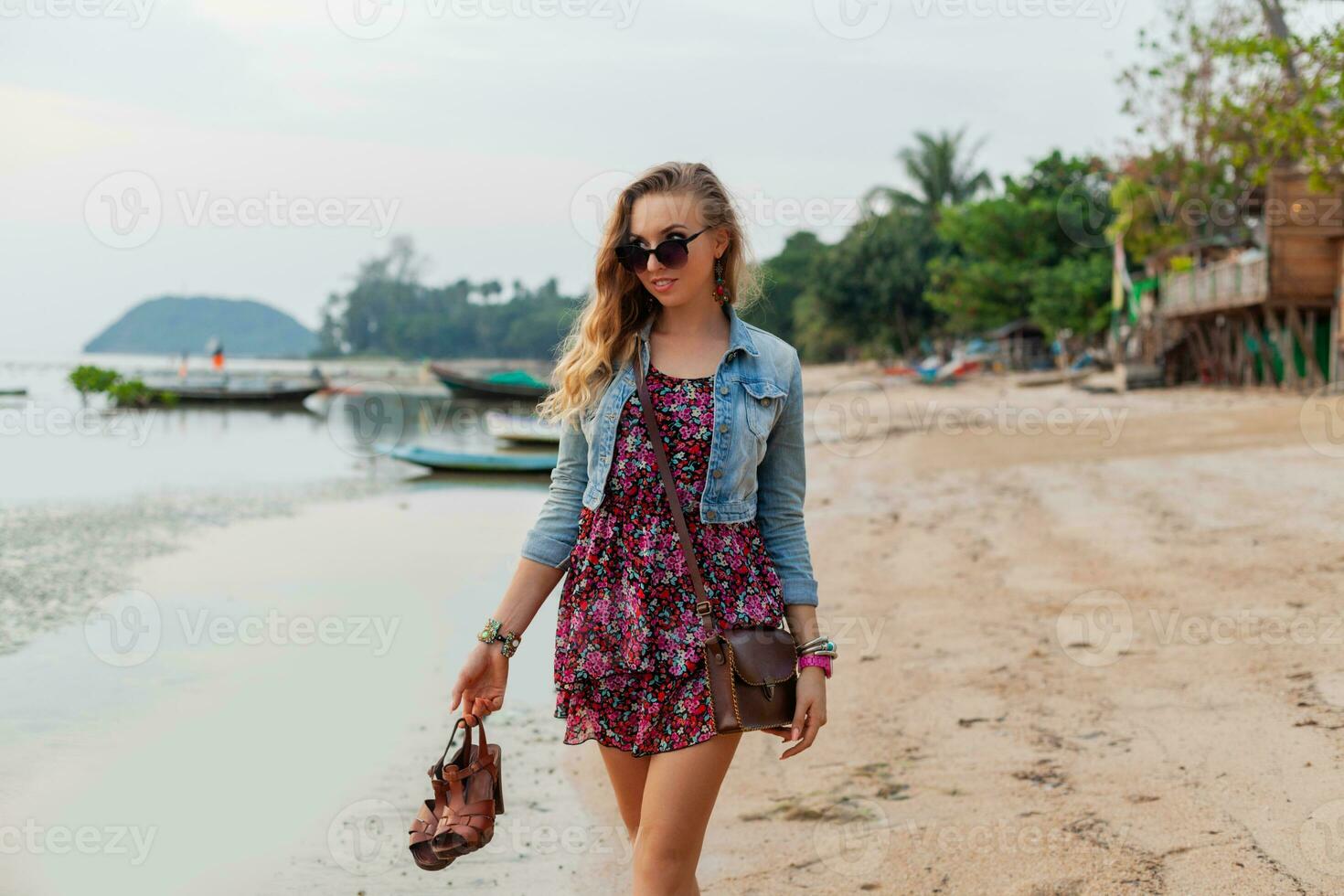 elegante donna nel estate vestito vacanza a piedi su spiaggia con scarpe nel mano foto