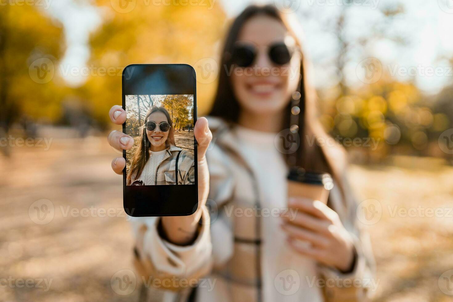attraente giovane donna a piedi nel autunno indossare giacca utilizzando Telefono foto