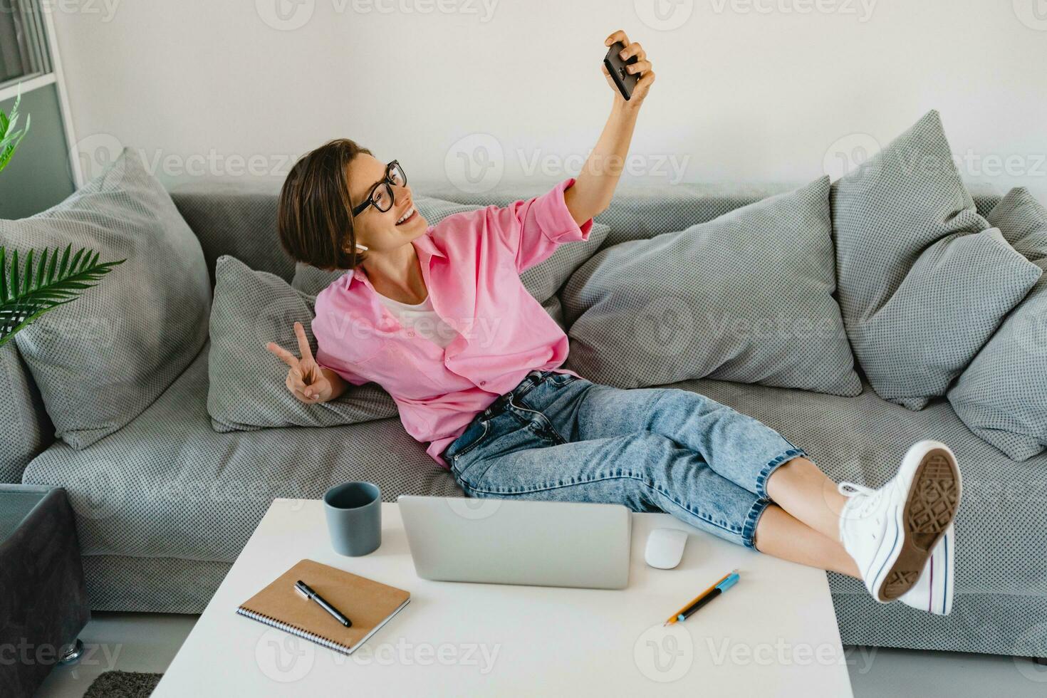attraente sorridente donna nel rosa camicia seduta rilassato su divano a casa a tavolo Lavorando in linea foto
