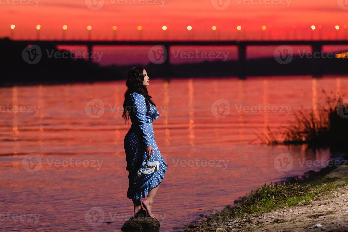 bella ragazza con lunghi capelli ondulati scuri in piedi sulla riva del fiume foto