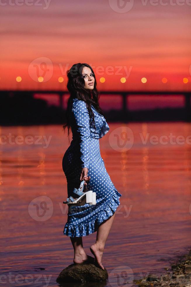 bella ragazza con lunghi capelli ondulati scuri in piedi sulla riva del fiume foto