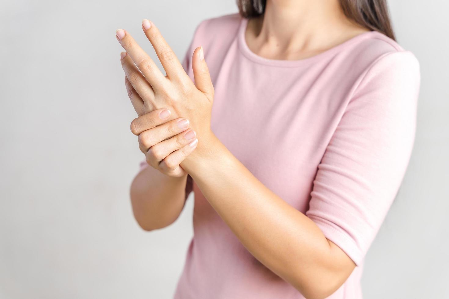 primo piano la giovane donna tiene il polso su sfondo bianco. ferita alla mano, sensazione di dolore. assistenza sanitaria e concetto medico. foto