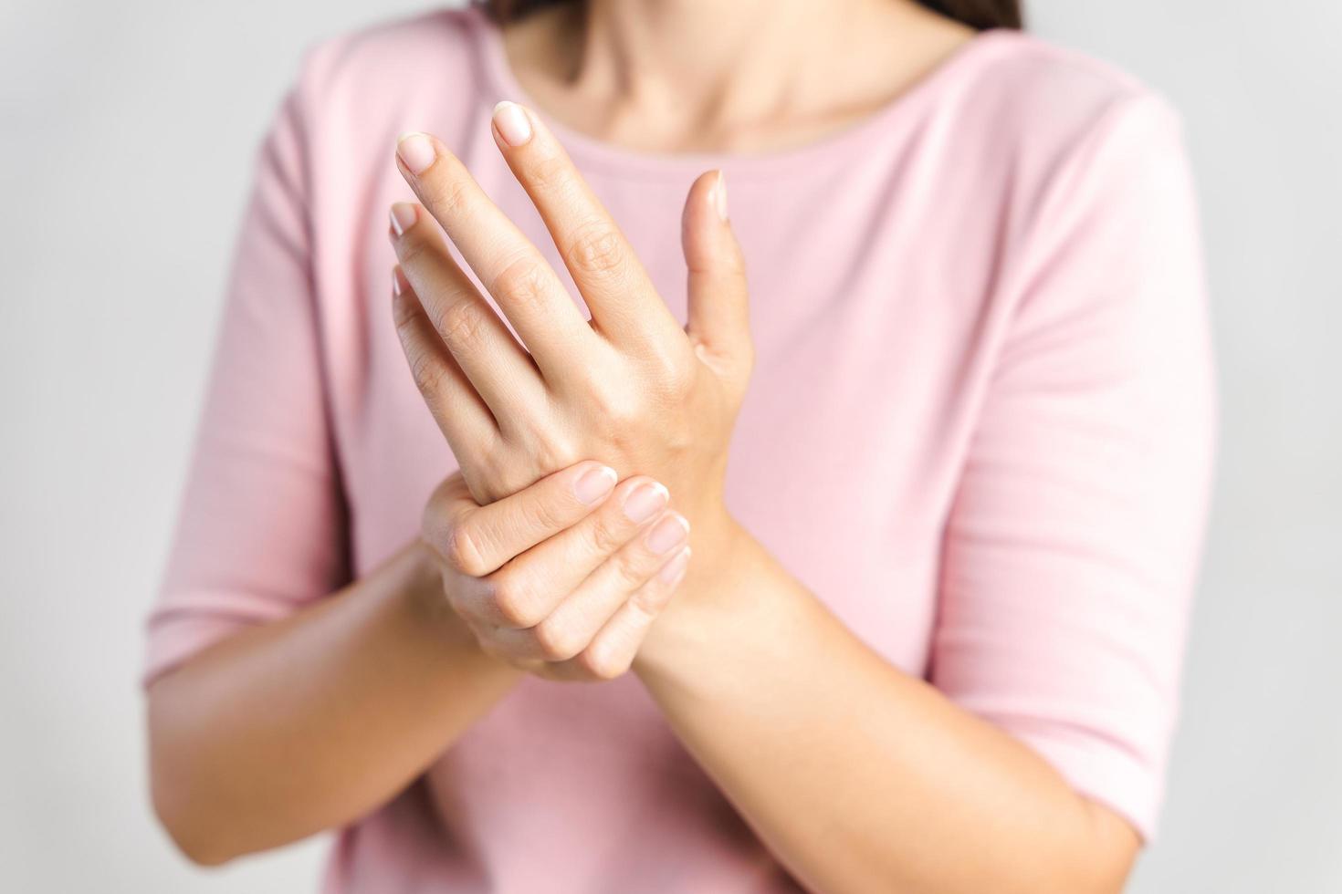 primo piano la giovane donna tiene il polso su sfondo bianco. ferita alla mano, sensazione di dolore. assistenza sanitaria e concetto medico. foto