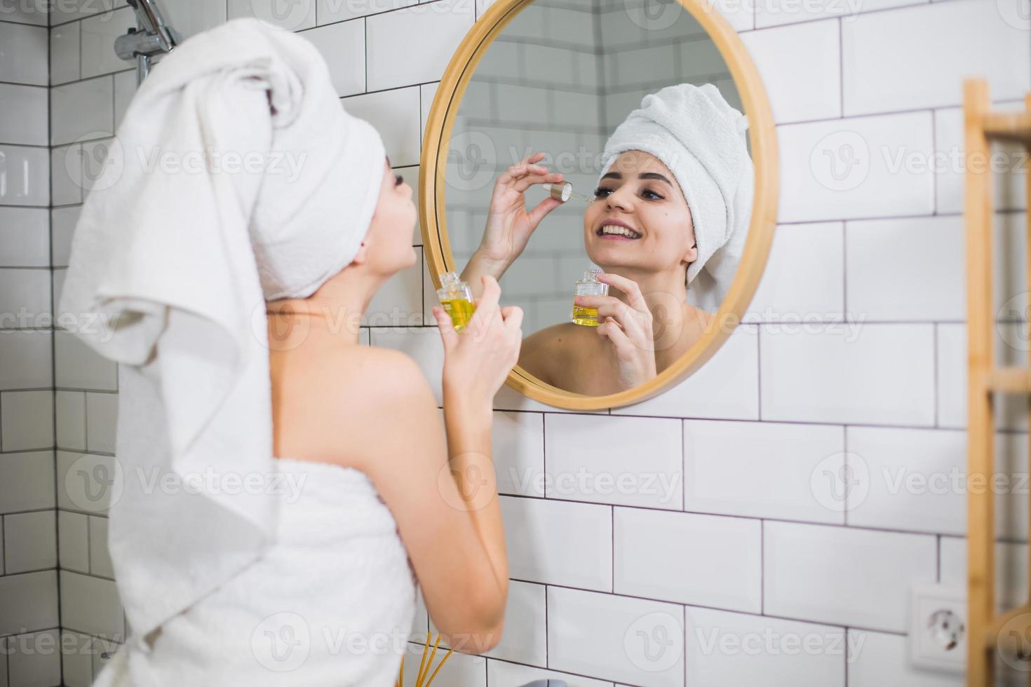 giovane donna in un asciugamano bianco applica olio idratante sulla pelle del viso. foto