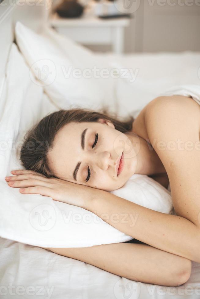 giovane donna che dorme pacificamente in camera da letto con lenzuola bianche fresche foto