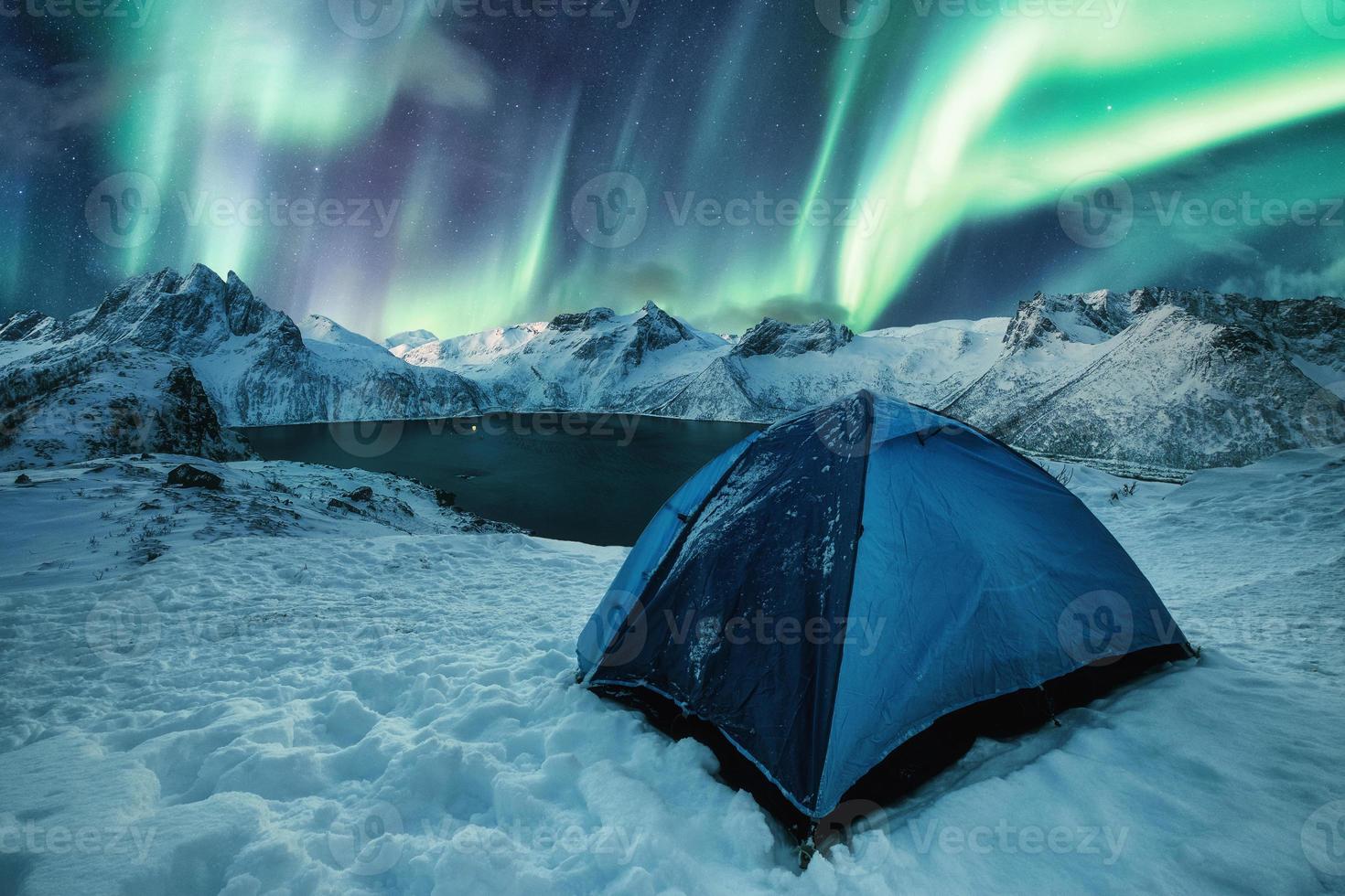 tenda blu che si accampa sulla collina innevata con l'aurora boreale che balla sulla catena montuosa nell'isola di senja foto