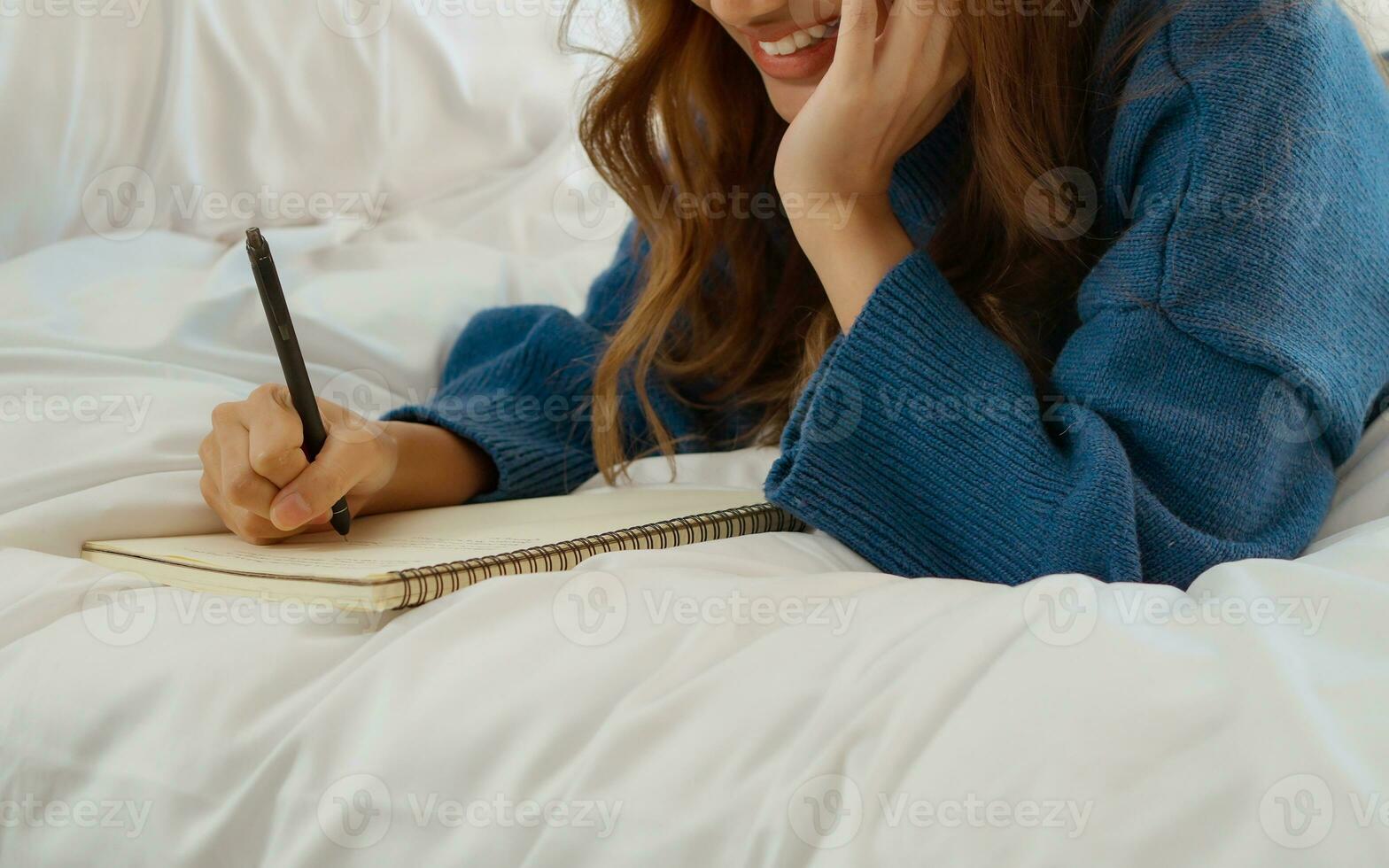 contento giovane donna posa su letto e scrittura nel rivista a Camera da letto. foto