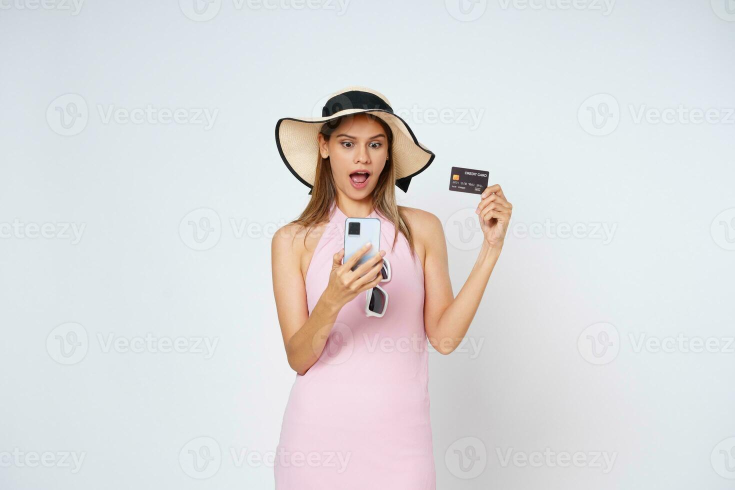 eccitato giovane donna mostrando credito carta mentre Tenere mobile Telefono isolato bianca sfondo. foto
